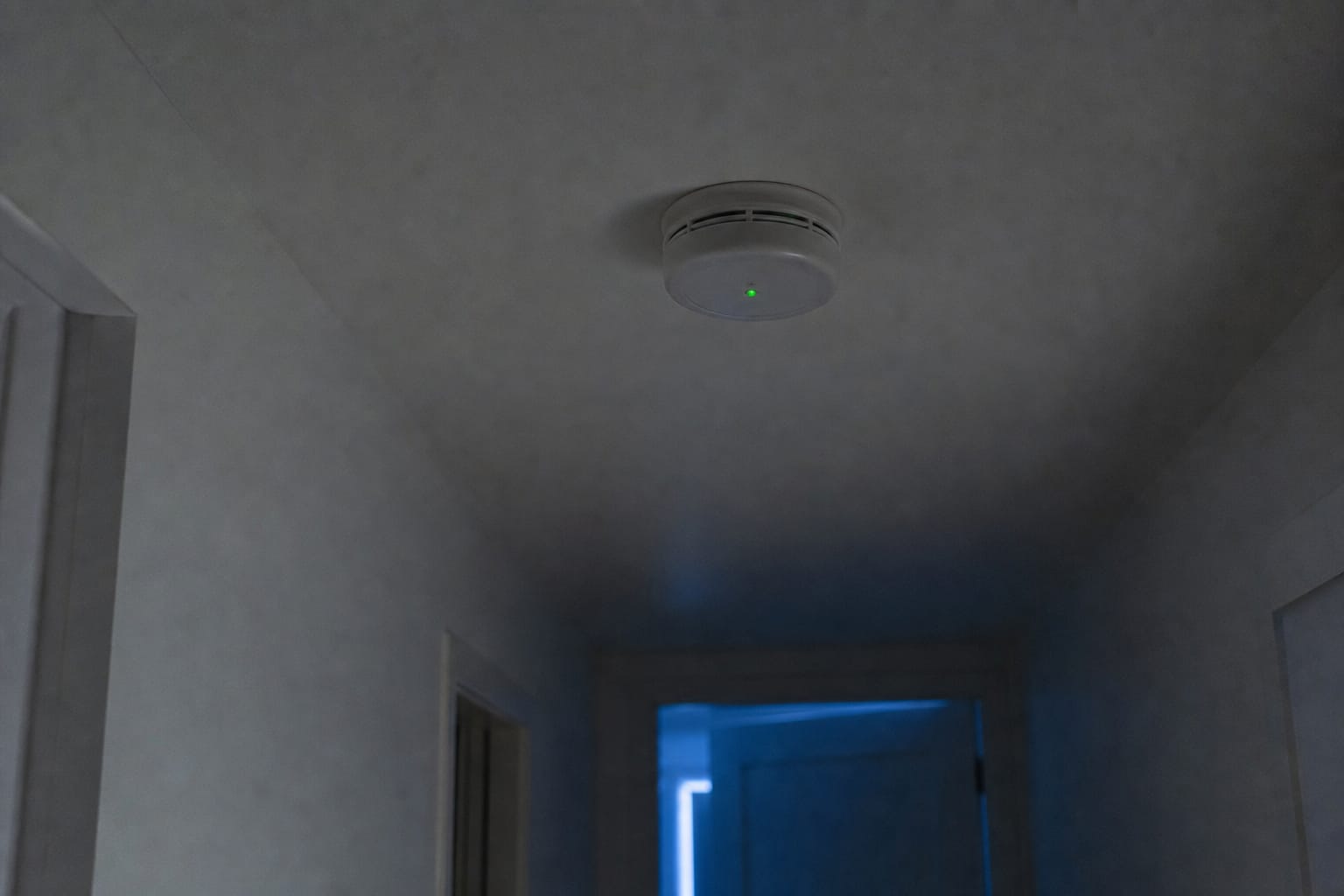 Détecteur de fumée blanc fixé au plafond d'un couloir sombre, petit voyant lumineux allumé au milieu de la nuit