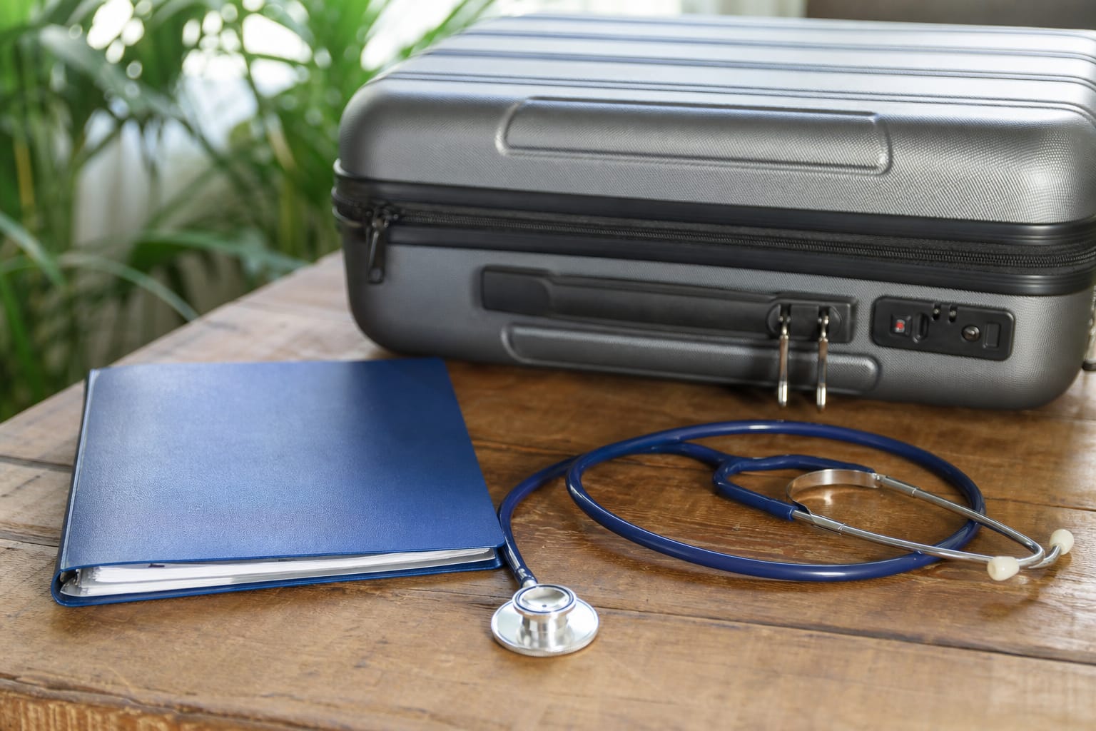 Valise de voyage fermée posée à côté d'un stéthoscope et d'un carnet de santé sur une table