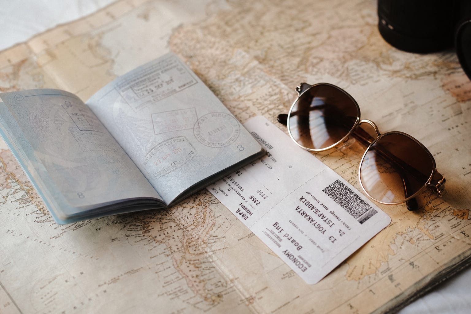 Passeport ouvert posé sur une carte du monde, à côté d'un billet d'avion et de lunettes de soleil