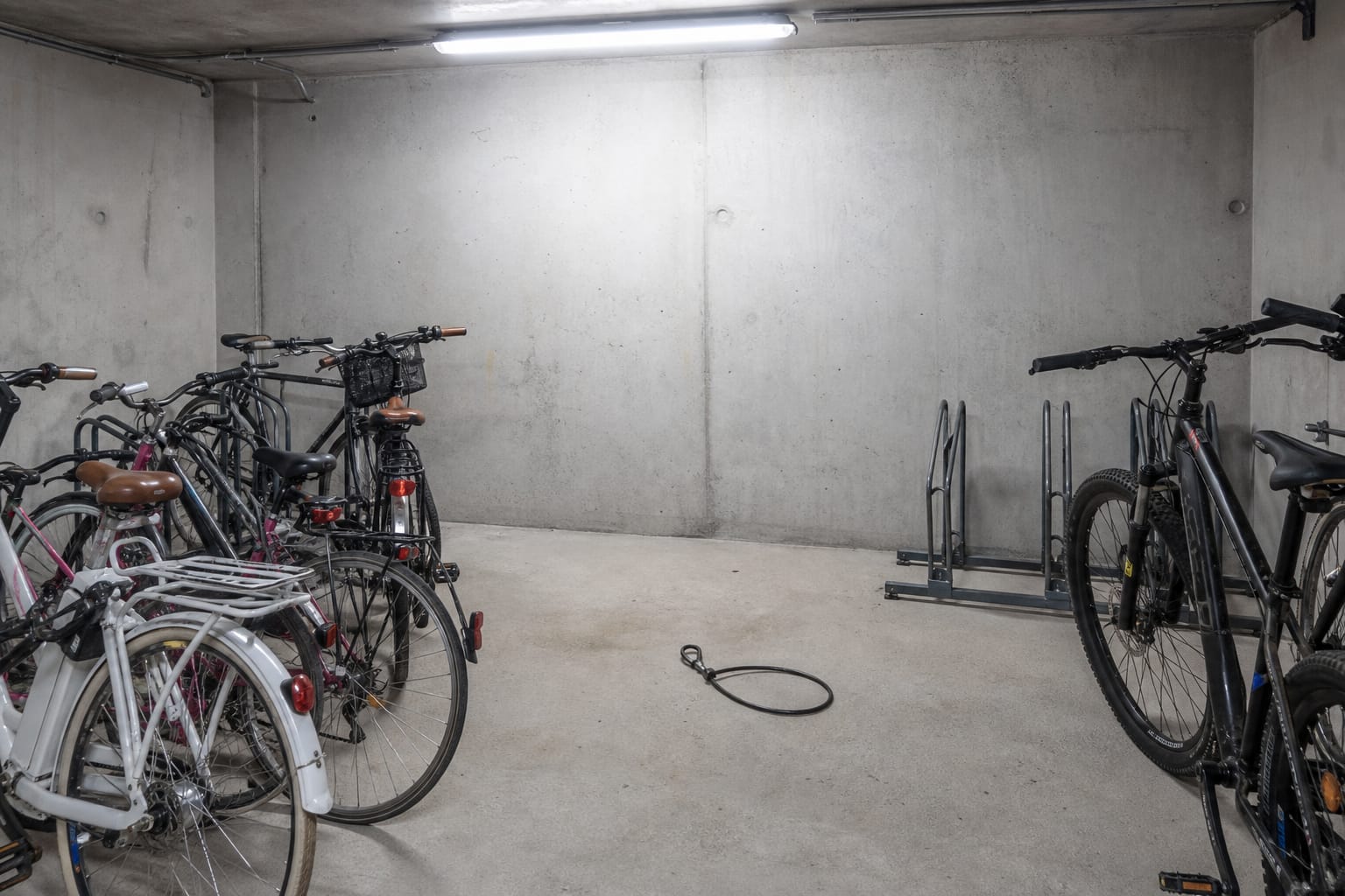 Local vélos en sous-sol d'un immeuble avec plusieurs vélos rangés et un câble antivol coupé abandonné au sol à la place vide