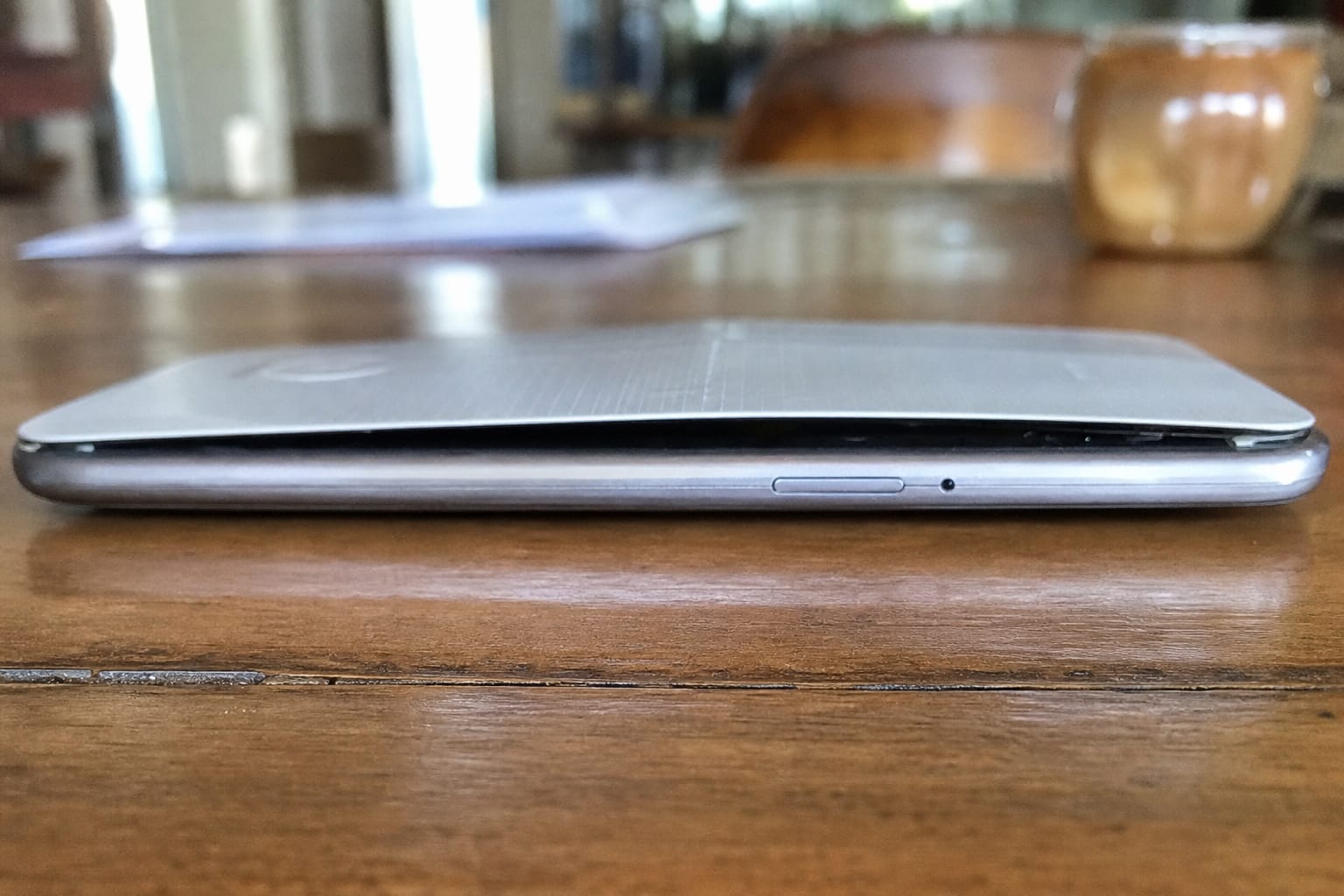 Smartphone posé sur une table en bois dont la coque arrière est bombée et décollée du châssis à cause d'une batterie gonflée