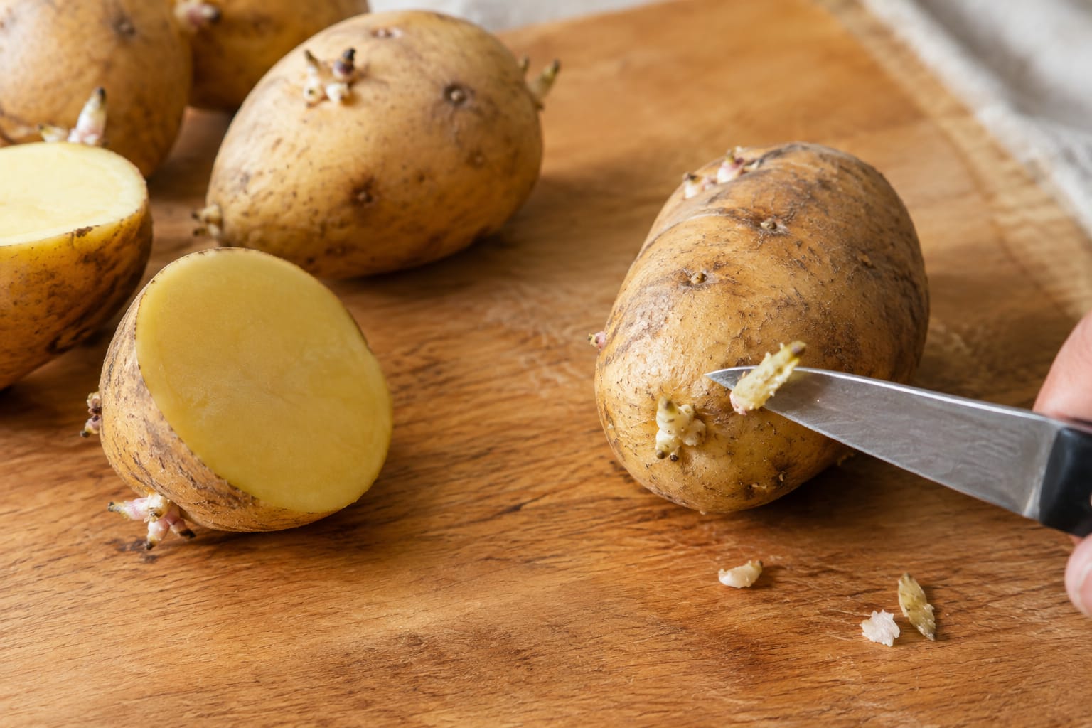 Pommes de terre avec de petits germes sur une planche en bois, une coupée en deux et une autre dont on retire un germe au couteau